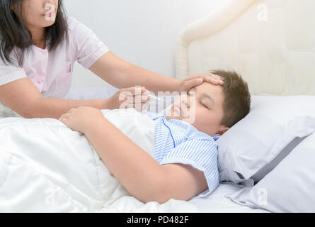 Mutter Temperaturmessung von ihr krankes Kind. Kranker Junge mit Thermometer Festlegung auf dem Bett und Mutter Hand, denn Temperatur. Krankes Kind mit Fieber und Kranke Stockfoto