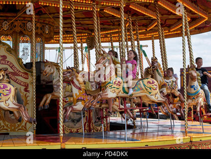 Kinder auf einem galoppierenden Pferd Karussell, Messegelände fahren Steam Fair. England Stockfoto