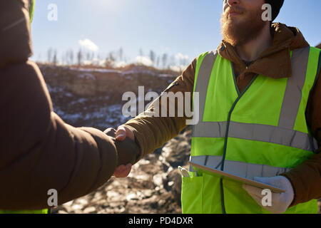 Den mittleren Abschnitt Portrait von bärtigen Industriearbeiter Tragekomfort reflektierende Jacke Schütteln mit Partner im Freien Stockfoto