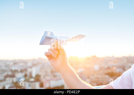 Der Mann hält Papierflieger in blauer Himmel bei Sonnenuntergang Licht mit Stadt Landschaft Hintergrund. Träume und Freiheit Konzept. Selektive konzentrieren. Copyspace Stockfoto