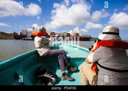 Zwei Touristen in einem kleinen Boot fotografieren ein großes Schiff in den Panamakanal, Republik Panama. Stockfoto