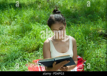 Ein Mädchen sitzt auf dem Gras und liest ein Buch Stockfoto