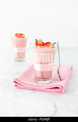 Zwei highball Trinkgläser mit rosa Schleife dekoriert und mit hausgemachten Erdbeer Mousse auf einem rosa Tuch und weißem Marmor Hintergrund gefüllt. Stockfoto