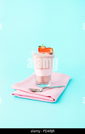 Selbstgemachte Erdbeer Mousse in ein Glas mit frischen Erdbeeren und eine rosa Schleife dekoriert, auf hellblauem Hintergrund. Stockfoto