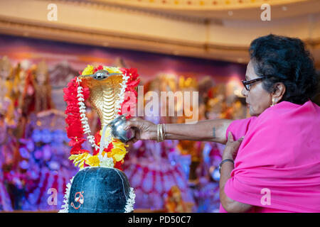 Eine Frau gießt Milch auf die Statue der Gottheit Shiva zu einem Hindu Tempel in South Richmond Hill, Queens, New York. Stockfoto