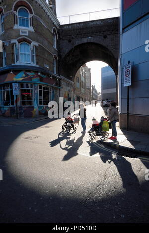 Menschen gehen auf der sonnigen Teil der Straße unter Eisenbahnbrücke in Brixton, London Stockfoto