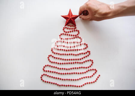 Eine Person macht eine kreative Weihnachten oder Neujahr Baum der Perlen in einem minimalistischen Stil gefertigt und verziert mit einem Stern. Celebratory Konzept oder eine kreative Idee oder Kreativität. Stockfoto