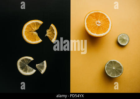 Zitrusfrüchte auf schwarzem und gelbem Hintergrund. Viele Schichten von Zitrone, Orange, Limette beieinander liegen. Viele Früchte. Vitamine und einen gesunden Snack. Stockfoto