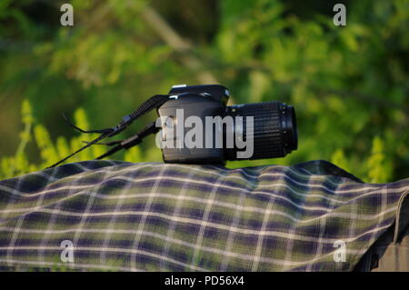 Kamera ruht auf Green Tartan eines Fotografen Shirt, als er auf dem River Exe Bank liegt. Exeter, Devon, Großbritannien. Stockfoto