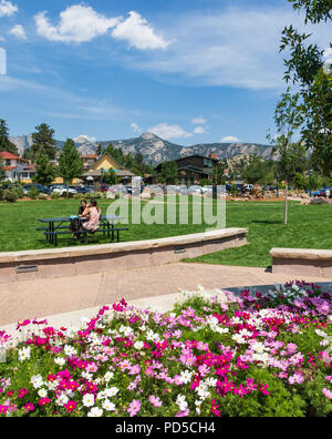 ESTES PARK, CO, USA-18 Juli 18: Zwei junge Frauen sitzen an einem Tisch für Picknick mit hell-rosa Blüten im Vordergrund, und die Rocky Mountains darüber hinaus. Stockfoto