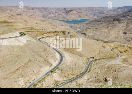 Kurvige asphaltierte Straße durch die Wüste und das Tal mit einem blauen See im Hintergrund Stockfoto