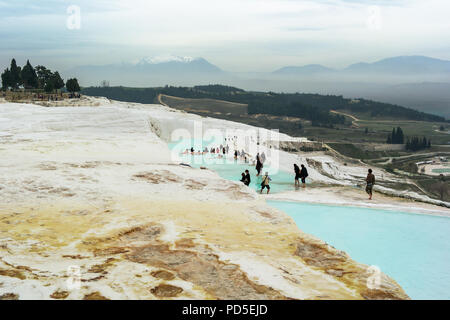 Ein Blick über die Terrassen von Pamukkale Travertin und die Badebecken mit Touristen ein Cluster von Bäume mit Schnee bedeckte Berge im Hintergrund. Pam Stockfoto