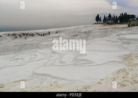 Ein Blick über die Terrassen von Pamukkale Travertin zu einigen Ruinen und ein Cluster von Bäume mit Schnee bedeckte Berge im Hintergrund. Pamukkale, Türkei. Stockfoto