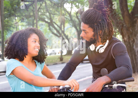 Biker spricht mit schwarze Frau auf dem Bürgersteig. Freunde Chatten in bewaldeten Straße. Stockfoto