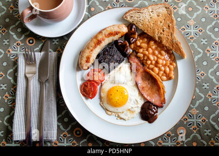 Ein hausgemachtes englisches Frühstück mit Ei, Speck, Cumberland Würstchen, Blutwurst, gebackene Bohnen, Tomaten, Pilze, Toast und eine Tasse Kaffee. Stockfoto