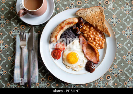 Ein hausgemachtes englisches Frühstück mit Ei, Speck, Cumberland Würstchen, Blutwurst, gebackene Bohnen, Tomaten, Pilze, Toast und eine Tasse Kaffee. Stockfoto