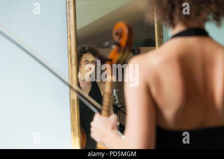 Schöne Frau mit Cello, in einem Spiegel sich selbst Stockfoto