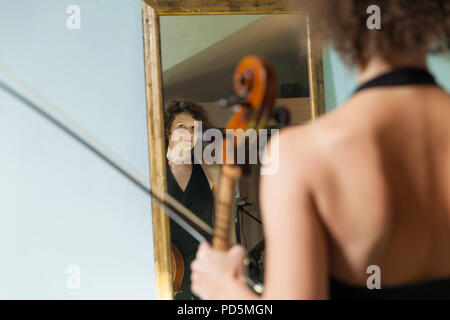 Schöne Frau mit Cello, in einem Spiegel sich selbst Stockfoto