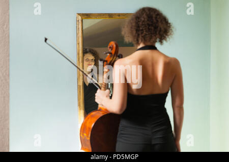 Schöne Frau mit Cello, in einem Spiegel sich selbst Stockfoto