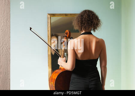 Schöne Frau mit Cello, in einem Spiegel sich selbst Stockfoto