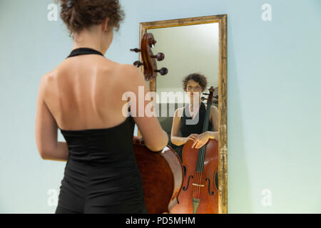 Schöne Frau mit Cello, in einem Spiegel sich selbst Stockfoto