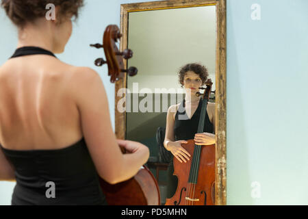 Schöne Frau mit Cello, in einem Spiegel sich selbst Stockfoto