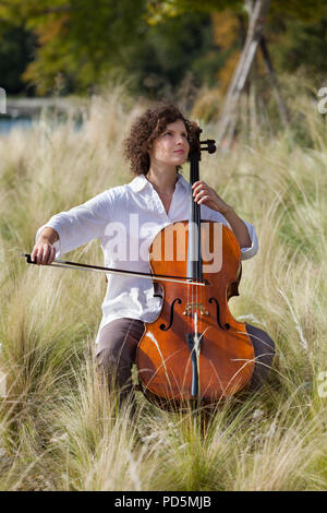Frau spielt das Cello zwischen Feldern Stockfoto