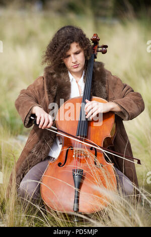 Frau spielt das Cello zwischen Feldern Stockfoto
