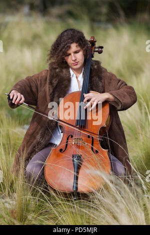 Frau spielt das Cello zwischen Feldern Stockfoto