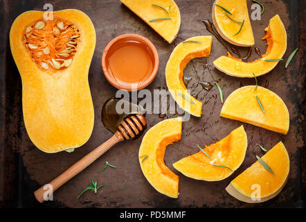 In Scheiben geschnittene rohe organische Butternut Squash auf das Backblech mit Honig und Rosmarin. Selektive konzentrieren. Im rustikalen Stil Stockfoto