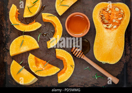 In Scheiben geschnittene rohe organische Butternut Squash auf das Backblech mit Honig und Rosmarin. Selektive konzentrieren. Im rustikalen Stil Stockfoto