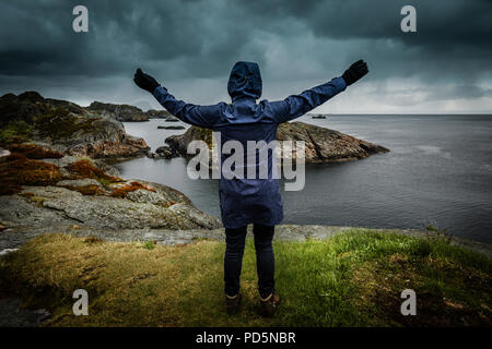 Einsame Person mit Waffen am Ufer eines Fjord, Kabelvag, Lofoten, Norwegen angehoben. Stockfoto