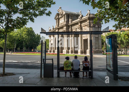 Madrid, Spanien - 4. August 2018: Alcala Tor oder Puerta de Alcala, drei Reisende an der Bushaltestelle warten, ist ein Monument, das sich in der Plaza de la Independenc Stockfoto