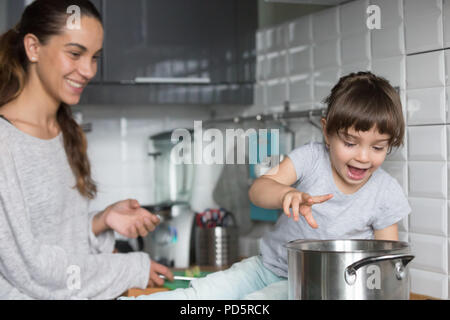 Neugierige Mädchen spielen mit Pot kochen mit Mama in der Küche Stockfoto