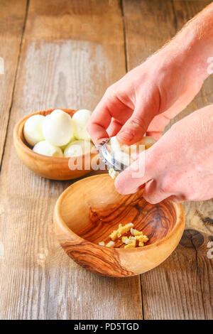 Männliche Hände Kraft der gekochtes Huhn Eier durch ein Gemüse Cutter für okroshki auf einem alten Holztisch. Schneiden Eier Stockfoto