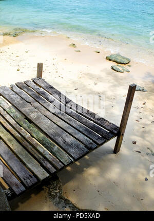 Eine kleine alte hölzerne Wetter geschlagen Angeln Jetty ruht auf einem klaren weißen Sandstrand am Ufer des türkisfarbenen blau, die Sonne scheint, einem typischen Stockfoto