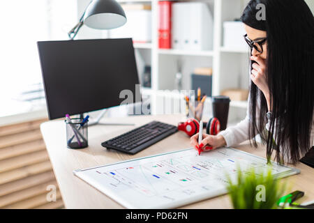 Ein junges Mädchen in Gläser steht in der Nähe des Tisches, hält einen Marker in die Hand und stützt sich auf eine Magnetplatte. Stockfoto