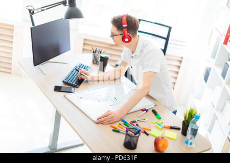 Ein junger Mann mit Brille und Kopfhörer steht in der Nähe ein Computer Schreibtisch, hält einen Marker in der Hand und druckt auf der Tastatur. Vor ihm liegt eine Magnetplatte und Markierungen. Stockfoto