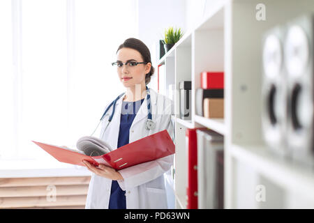 Eine schöne, junge Mädchen in einem weißen Gewand steht in der Nähe der Unterschlupf und Spiegelungen, die durch einen roten Ordner mit Dokumenten. Stockfoto