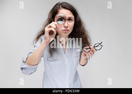 Junge brünette Mädchen mit Brille. Ein Mädchen schaut durch ein Vergrößerungsglas. Stockfoto