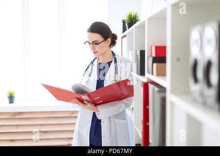 Eine schöne, junge Mädchen in einem weißen Gewand steht in der Nähe der Unterschlupf und Spiegelungen, die durch einen roten Ordner mit Dokumenten. Stockfoto