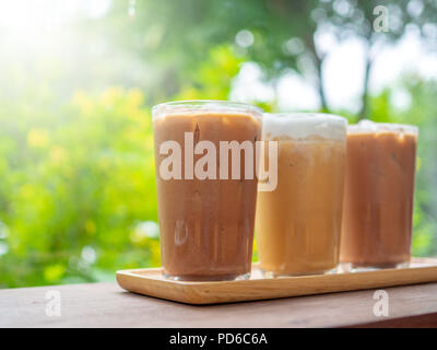Drei Gläser Eiskaffee auf Holztisch auf grünen Garten Hintergrund im Cafe. Stockfoto