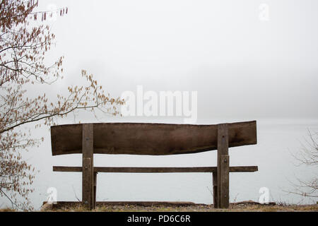 Leeren Bank am Rande eines Sees im Herbst Symbol für serenety Stück Ruhe und Meditation foggy nebligen Tag über dem Wasser Stockfoto