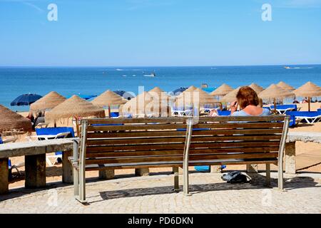 Frau sitzen auf einer Bank mit Blick auf den Strand, Albufeira, Portugal, Europa. Stockfoto