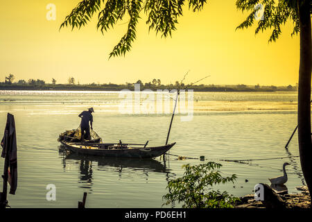 Ein Fischer bereitet sein Netz auf seinem Boot als Dock watet um an Land. Insel Cam Kim am Ufer. Hoi An VN Stockfoto