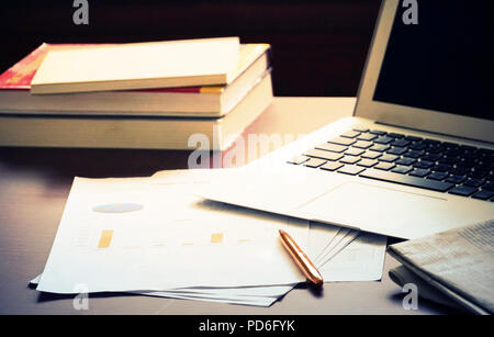 Die Tabelle, die Papier und Stift und Zeitung und Notebook haben und Stapel von Büchern. Stockfoto