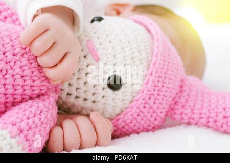 Neugeborenes Baby schläft mit einem rosa Spielzeug Baby und Hände hug Stockfoto