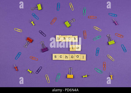 Zurück zu Schule text auf Holz Buchstaben auf lila Hintergrund mit bunten Stationery items. Konzept für den Beginn des akademischen Jahres Stockfoto