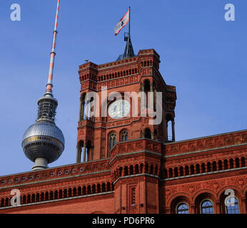 Berlins berühmtes rotes Rathaus mit kunstvollem Uhrenturm überblickt den öffentlichen Platz, auf dem sich Besucher bei Sonnenschein auf Bänken entspannen Stockfoto