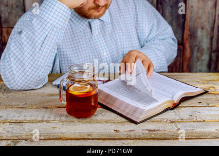 Ein Mann mittleren Alters an einem Tisch sitzen die Bibel lesen Stockfoto